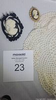 Two cameo pins and a handmade lace doily displayed on a flat surface for identification.