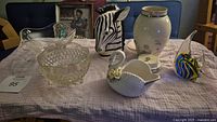 Wide view of lot items on table showing all pieces including swan bowl, zebra vase, clear hobnail bowl, musical jar, art glass fish, cream floral vase