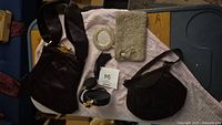 Photo showing two black vintage handbags, silver-tone beaded clutch, matching beaded mirror compact, and black refillable perfume bottle with puffer atomizer on cloth-covered surface.
