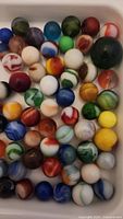 Top-down photo showing a large assortment of colorful vintage marbles of various patterns and sizes inside a white container.