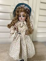 Full front view of 14-inch tall Kestner bisque head doll wearing floral dress and blue bonnet with lace and flowers.