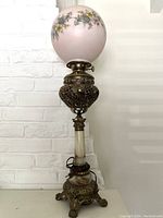 Full view of the oil lamp showing pink floral painted glass globe, brass filigree midsection, and onyx base with claw feet.