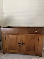 Front view of antique pine dry sink showing the open basin on the top left, drawer with white knob on the top right, and two paneled cabinet doors below with black metal latches.