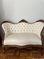 Full front view showing carved wood frame and cream tufted upholstery