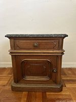 Front view of the Victorian nightstand showing the grey marble top, drawer, and cabinet door with metal knobs.