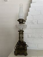 Full view of the antique Victorian pedestal oil lamp showing its ornate metal base, cut glass reservoir, and frosted chimney.