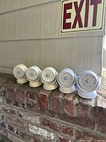 Five white round battery-operated motion sensor lights placed on a brick ledge under an exit sign, showing the front sensor and LED bulb array of each light.