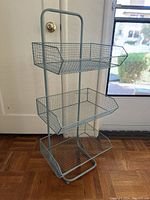 Front angle view of the blue metal over-the-door basket hanger showing all three baskets and the hook top.