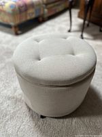 Round beige fabric footstool ottoman with tufted top shown closed.