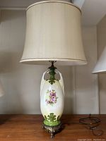 Full view of the lamp showing the beige fabric shade and the ceramic body with floral painting.