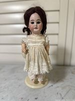 Front view of the vintage bisque head doll dressed in cream lace dress, showing facial features, mohair wig, and full outfit.