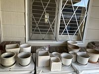 11 vintage ceramic planter pots arranged in a single row on a white washer/dryer unit, background window with bars.
