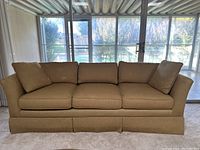 Full front view of the three-seat vintage sofa with beige fabric upholstery and removable cushions.