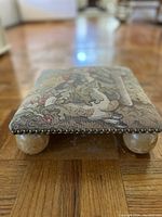 Close-up of the footstool showing upholstery pattern, metallic nail trim, and one crystal ball foot.