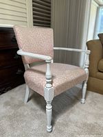 Side view of the vintage chair showing white wooden frame with turned leg and arm details, pink clamshell patterned upholstery on seat and back.