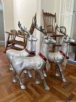 Front view of three silver Christmas reindeer standing on wooden floor, each with red collars and detailed antlers.