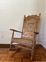 Front view of rocking chair showing carved back, spindle arms and cane seat