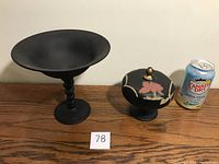 Two black satin glass compotes shown side by side with a soda can for size reference. One has a tall twisted stem and wide bowl, the other has a decorated lid with a floral design.