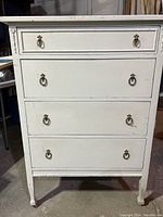 Front view of the antique dresser painted white showing four drawers with metal ring handles and decorative top edge.