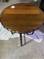 Top view of round wooden drop leaf table with scalloped edge and aged surface.