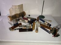 Multiple antique glass vials, some sealed with cork stoppers and some with metal lids, laid out on a surface with an old paper label in background. Varied sizes and colors of glass seen.