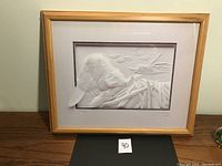 Framed paper relief art of beaver at dam by Calvin Nicholls displayed on wooden surface