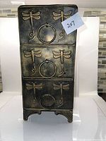 Front view of the metal dresser featuring three drawers with dragonfly embossing and ring handles.