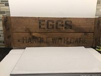 Front view of wooden sign board with 'EGGS HANDLE WITH CARE' text visible.
