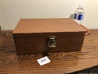 Closed view of rectangular brown leather travel bar case with metal latch and handle.