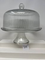 Glass cake covered dish on pedestal with ribbed texture and round knob on dome lid.