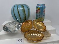 Lot of three glassware items including globe vase, faceted candle holder, and shell divided dish with soda can for scale.