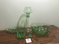 Five green Depression glass pieces displayed on wooden surface under neutral lighting