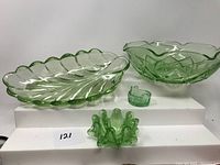Four green glass pieces on display including decorative bowls, small dish, and candle holder