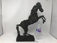 Full view of the rearing horse sculpture next to a water bottle for scale, showing wire and plaster construction and rectangular base.