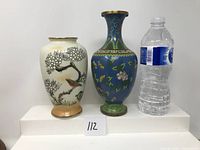 White and blue cloisonné vases placed side by side next to a water bottle for scale.