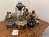 Group of 8 antique oil lamps placed on wooden surface, showing varying sizes and metal finishes.
