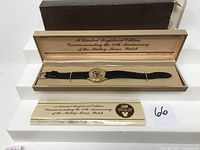 Full view of the watch in its original box with lid open and certificate card below it, displaying commemorative text and a sticker with lot number 66.