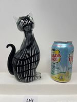 Front view of the black and white striped Murano glass cat figurine displayed next to a Canada Dry soda can for size reference.