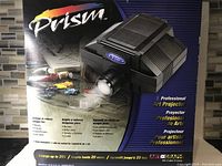 Box and art projector device showing branding, features and multilingual text describing the projector's capabilities.