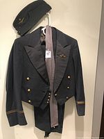 Front view of the RCAF jacket with gold buttons, satin lapels, chest badge, and matching side cap on a hanger against a white wall