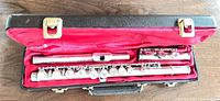 Image shows the three-piece silver plated E.M. Winston FL115S student flute laid in a black hard shell case lined with red satin fabric, case open exposing the flute components.