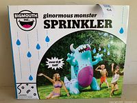 Front of original retail box showing colorful monster inflatable sprinkler illustration with children playing, brand and product name visible.