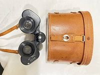 Front of Carl Seitz binoculars showing magnification and field of view markings alongside original tan leather case with strap and buckle.
