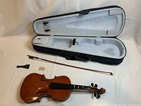 Violin disassembled with body, bow, bridge, tailpiece laid out next to open plush-lined hard shell case
