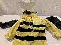 Plush yellow-and-black bee costume with hood and mesh wings laying flat on white surface showing front view