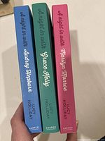 Spine view of three softcover books in the trilogy with distinct blue, green, and pink colors.