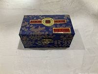 Closed royal blue brocade box with gold floral patterns and labels indicating 'Healthy Ball' and 'Made in China'.