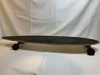 Side view of longboard skateboard with black grip tape top and black cruiser wheels on a white background.