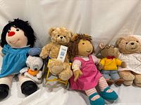 Seven vintage plush toys visible: Miss Molly's Dolly, D.W. Read, Tenderheart Bear, Heart-to-Heart Bear, Donald Duck puppet, and others aligned side by side on white backdrop