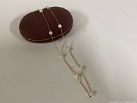 Necklace draped over a burgundy oval jewelry box showing gold chain and spaced pearls.